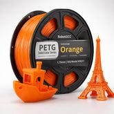 Spool of orange 3D printing filament with small models made from it on a white background