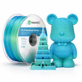 Spool of blue filament with a knitted bear and model building on a white background