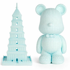 Light blue crochet teddy bear and Leaning Tower of Pisa model on a white background