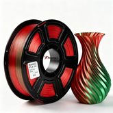 Spool of red and black filament next to a colorful vase on a white background