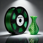 Spool of green filament labeled 'RobotGCC' next to a green glass vase on a reflective surface.