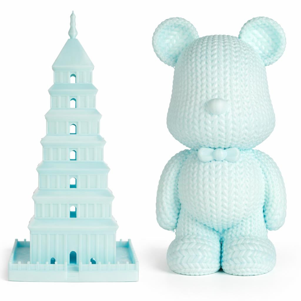 Light blue crochet teddy bear and Leaning Tower of Pisa model on a white background