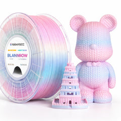 Spool of pink and blue filament with a pink and blue 3D printed tower and bear figure on a white background.