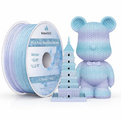 Spool of blue filament labeled 'RobotGCC' next to a knitted bear toy with a tower model.