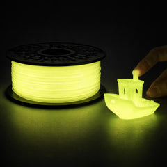 Spool of glowing green filament and a small 3D printed object on a dark background
